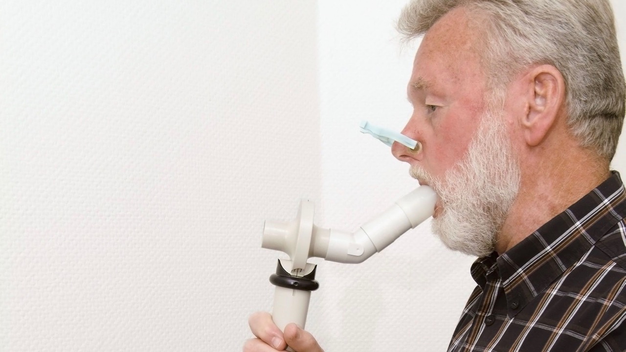 Mann trägt ein Nasenklammer und bläst in ein Spirometer
